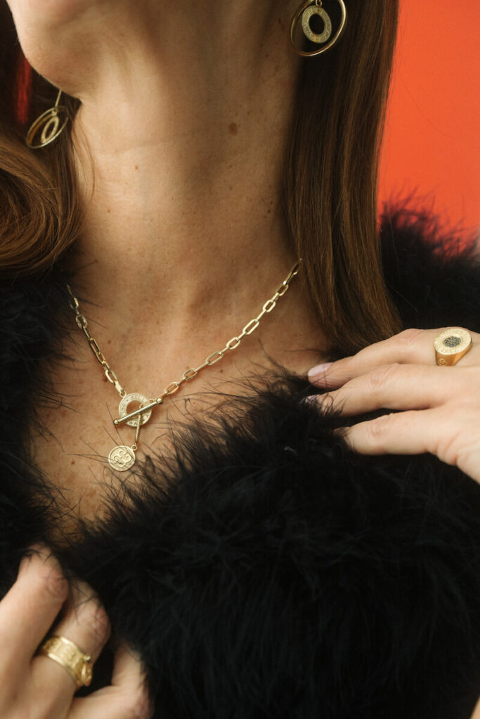 Fragment sylwetki kobiety ubranej na czarno ze złotym naszyjnikiem Belleway