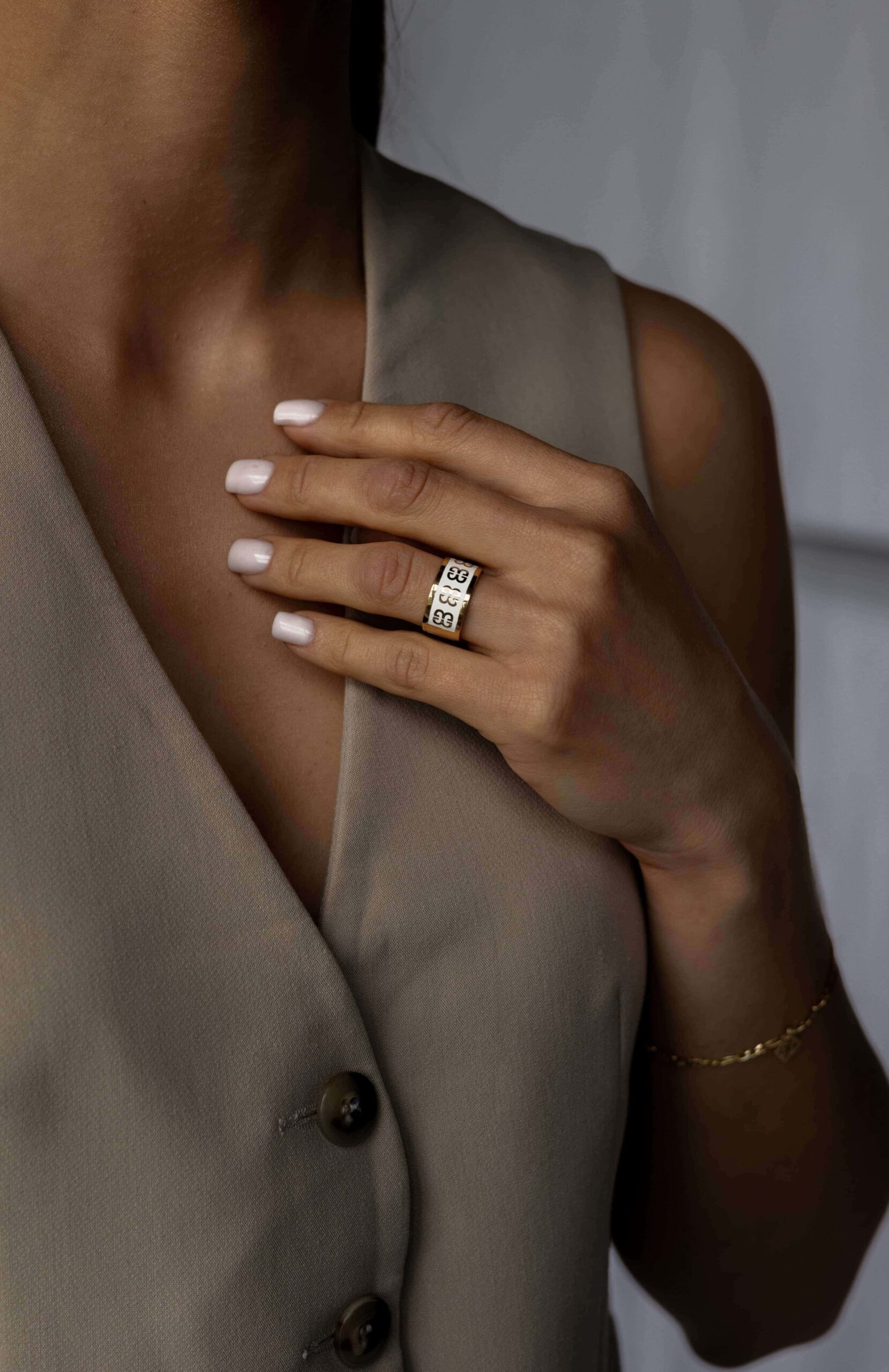 Złota obrączka z białą emalią na kobiecej dłoni położonej na beżowej kamizelce